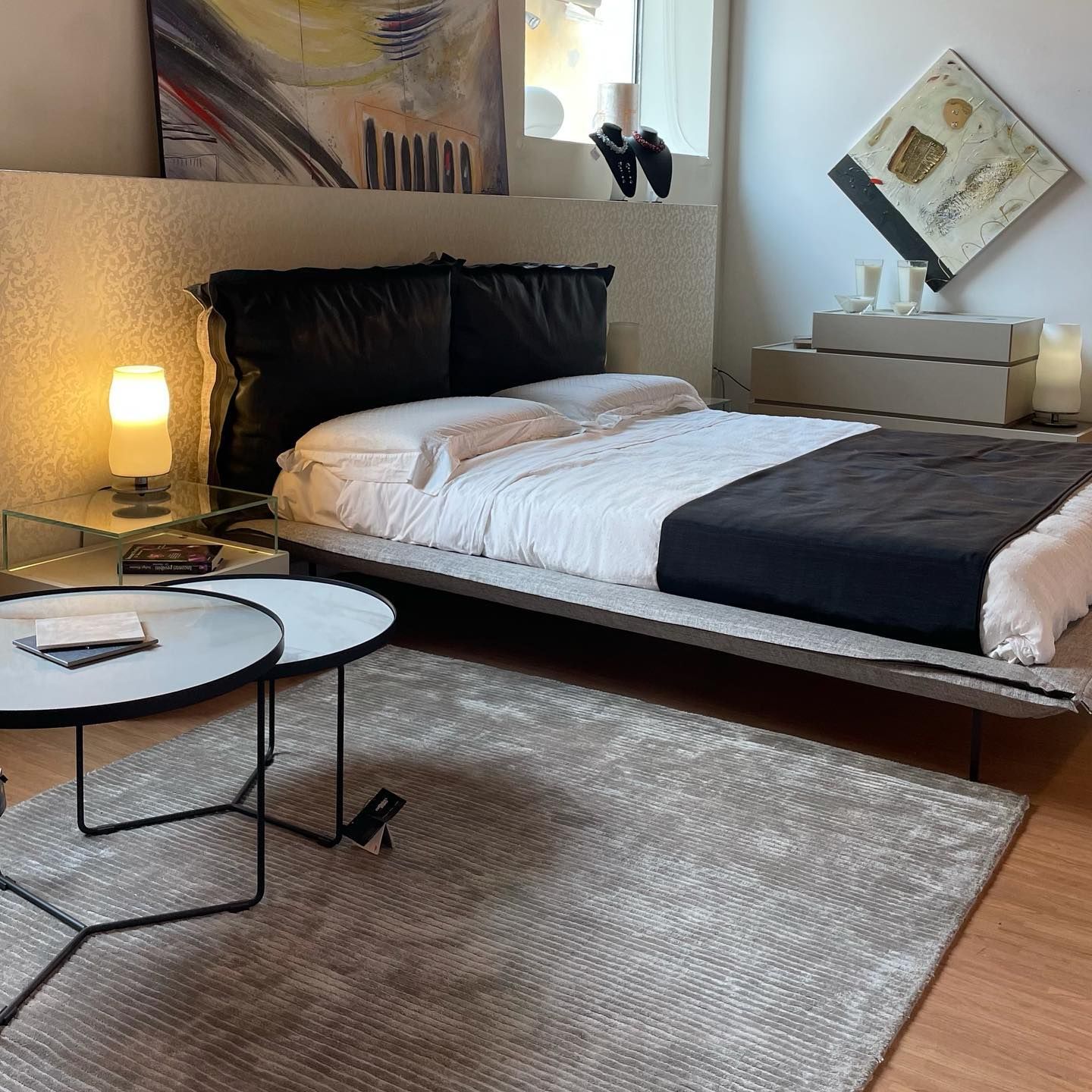 Camera da letto moderna con pareti grigie, letto, tappeto, quadri astratti e un tavolino.