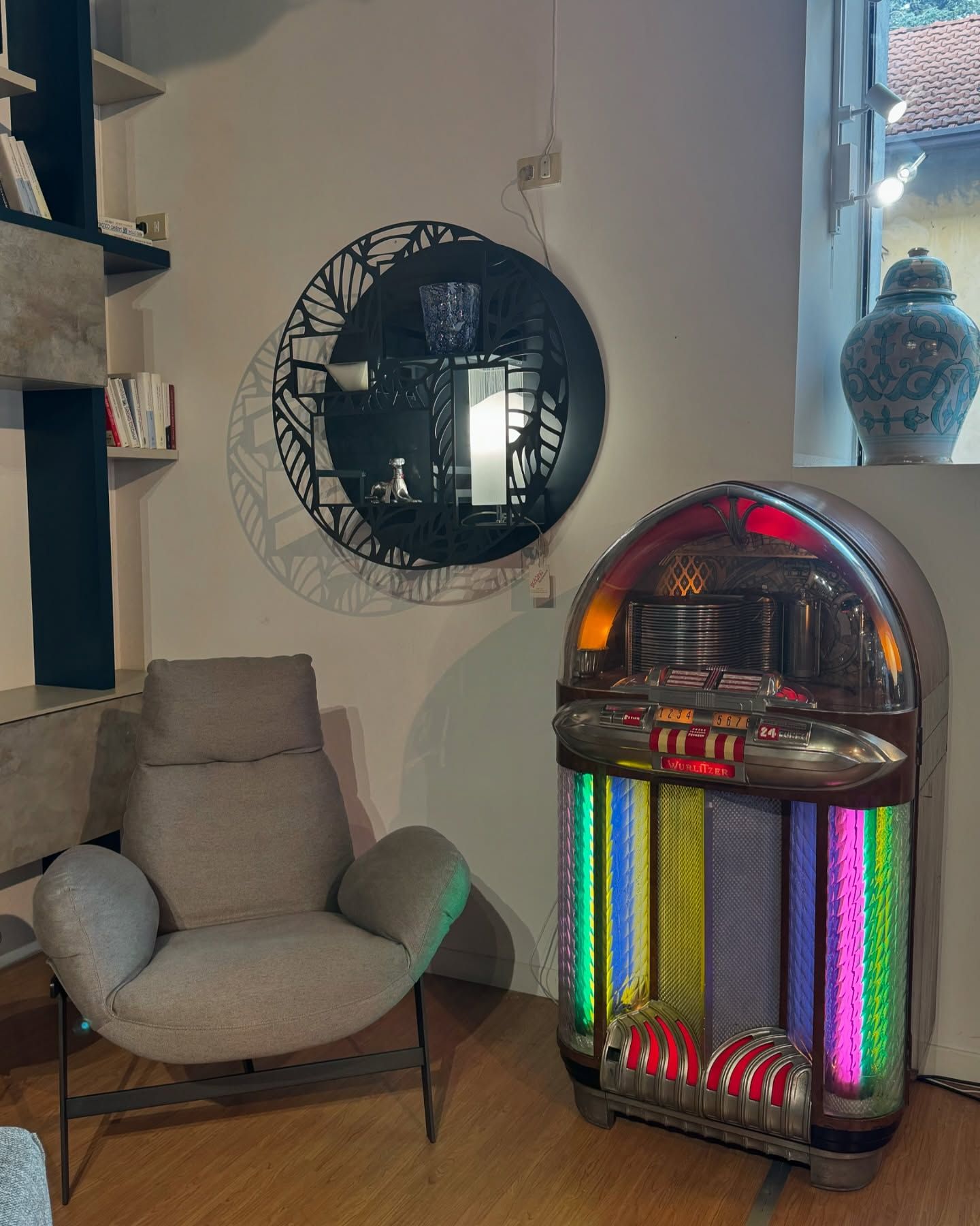 Camera accogliente con un jukebox d'epoca, una sedia moderna, uno specchio decorativo e un vaso antico vicino alla finestra.