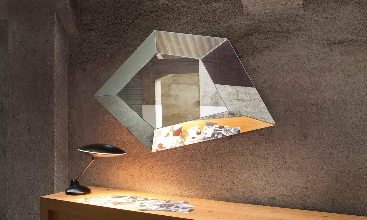Specchio geometrico su parete strutturata sopra una scrivania con lampada.