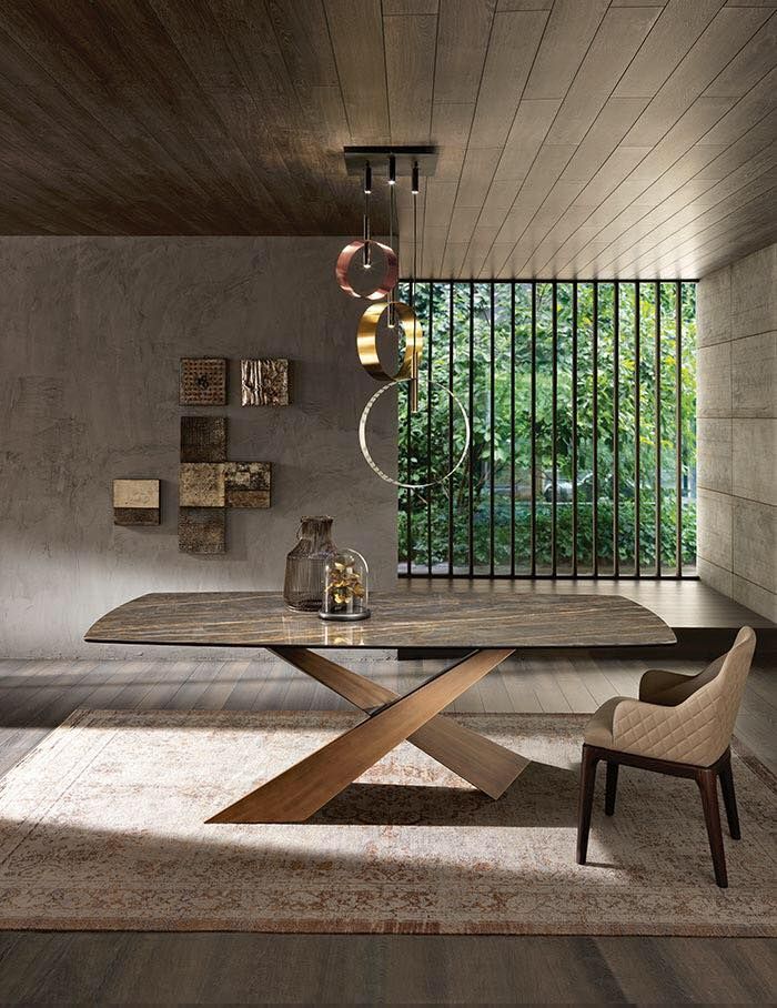 Sala da pranzo con grande tavolo, tappeto a fantasia, illuminazione moderna e vista sul verde attraverso una finestra.