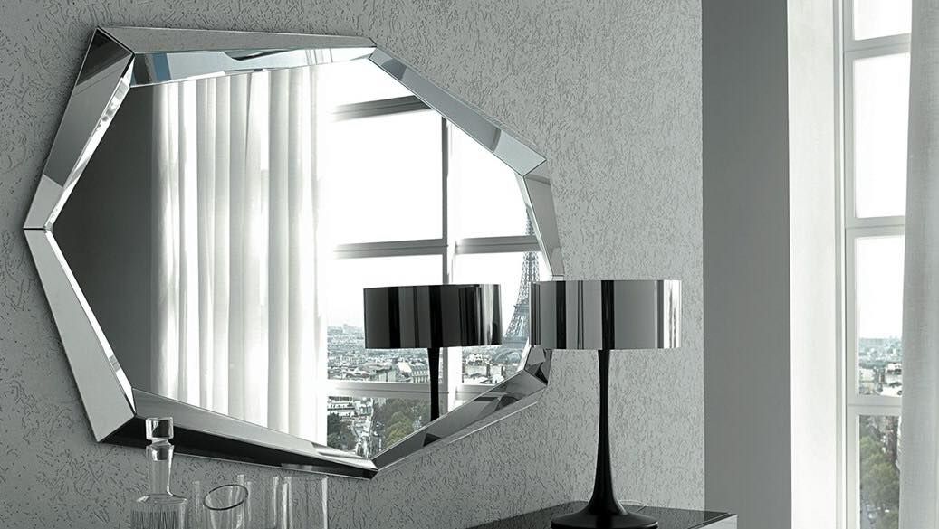 Specchio geometrico che riflette una stanza con una finestra, due lampade e una parete strutturata.