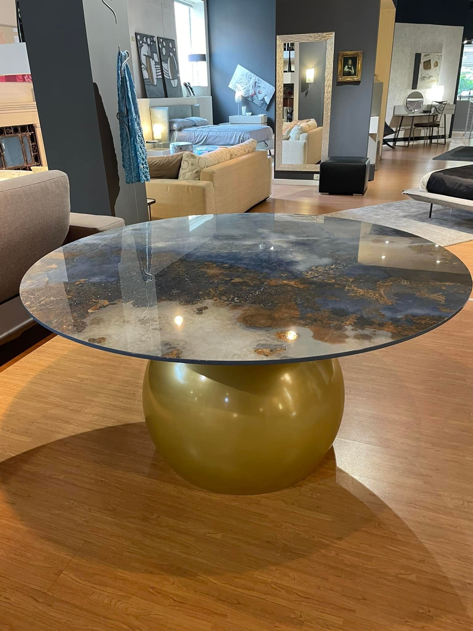 Tavolino rotondo con base dorata e piano in vetro decorato con un motivo blu e oro.