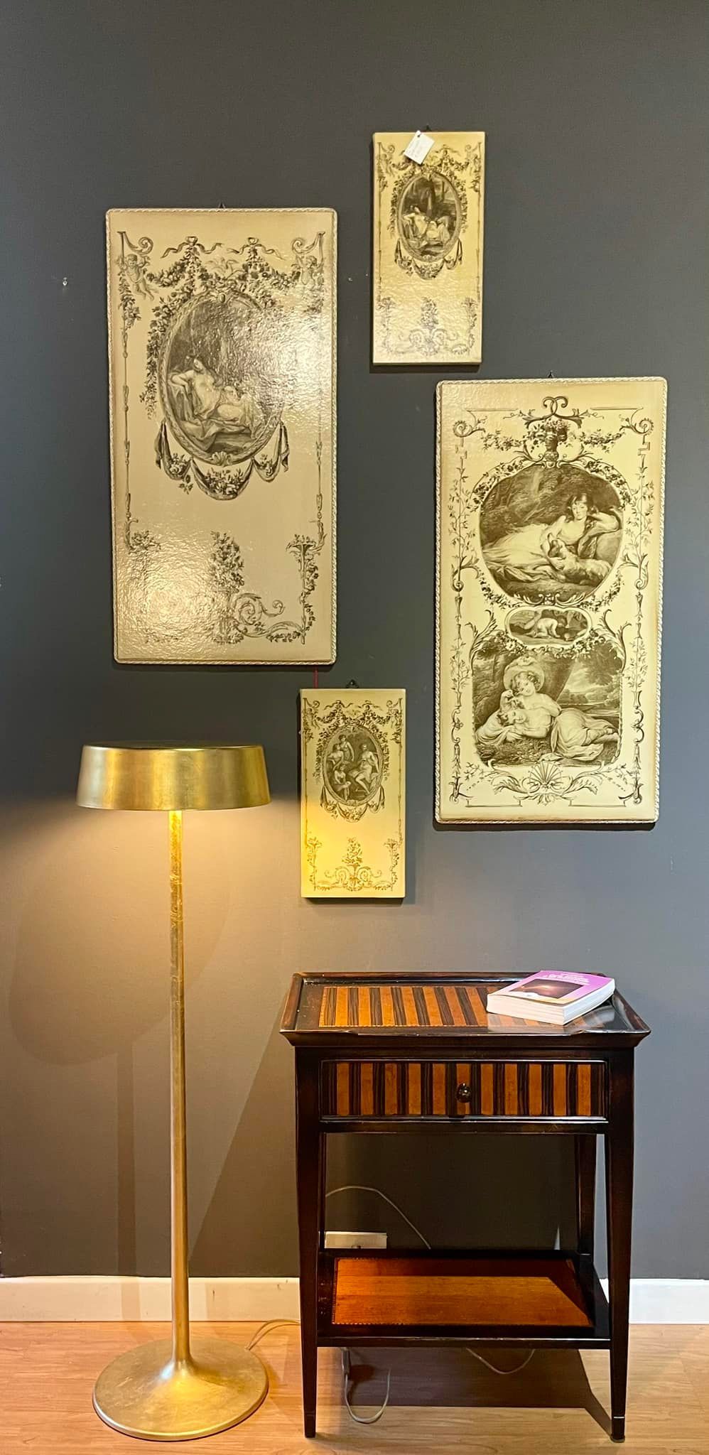 Una stanza con opere d'arte, una lampada e un tavolo di legno contro una parete grigio scuro.