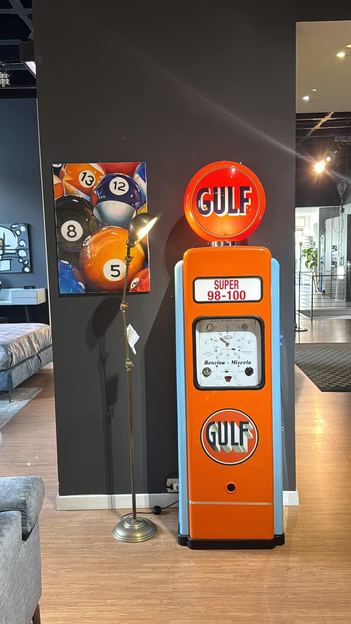 Pompa di benzina Orange Gulf e opera d'arte con palla da biliardo contro una parete grigia.