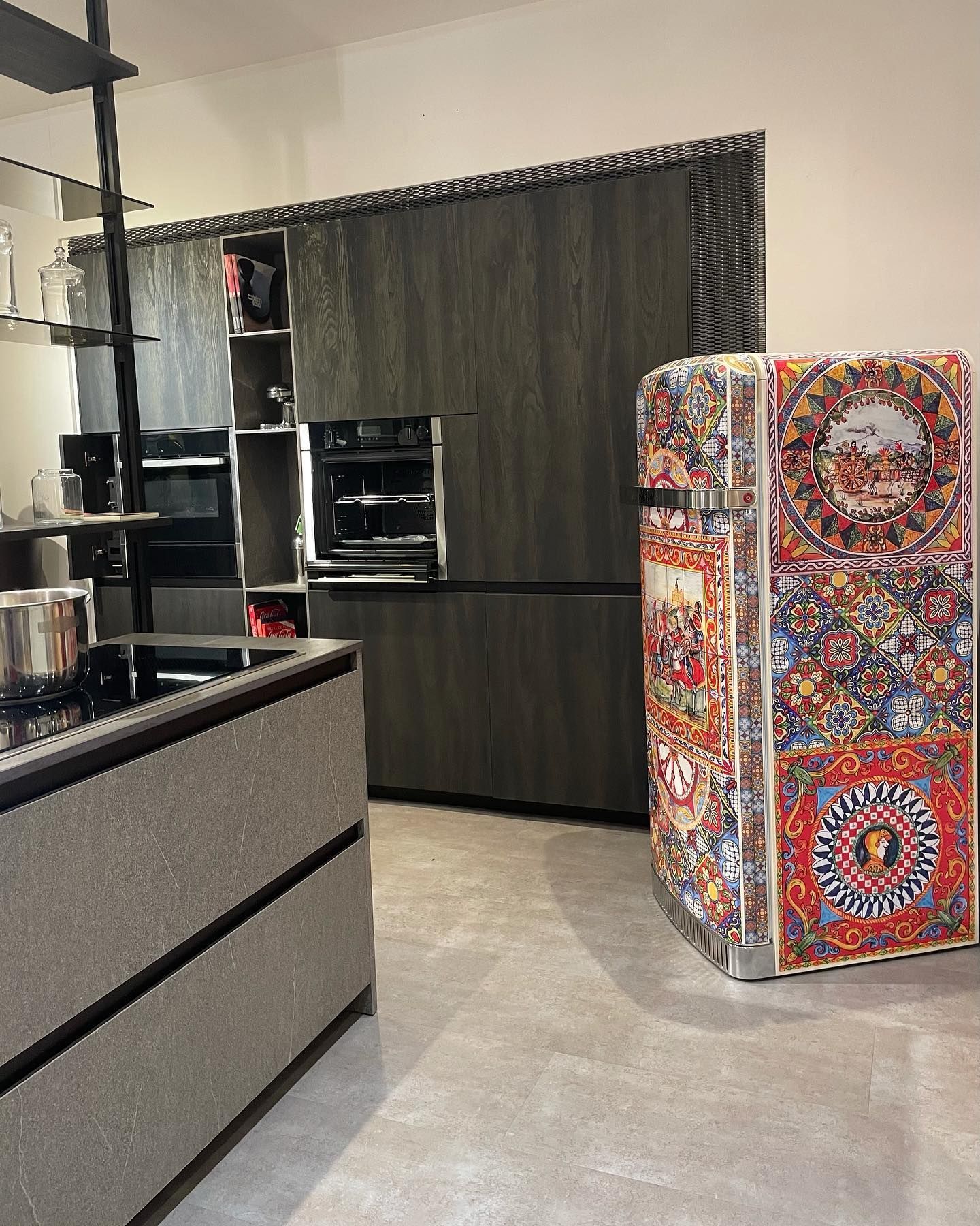 Cucina con frigorifero decorato, forni da incasso e isola con piano di lavoro grigio.