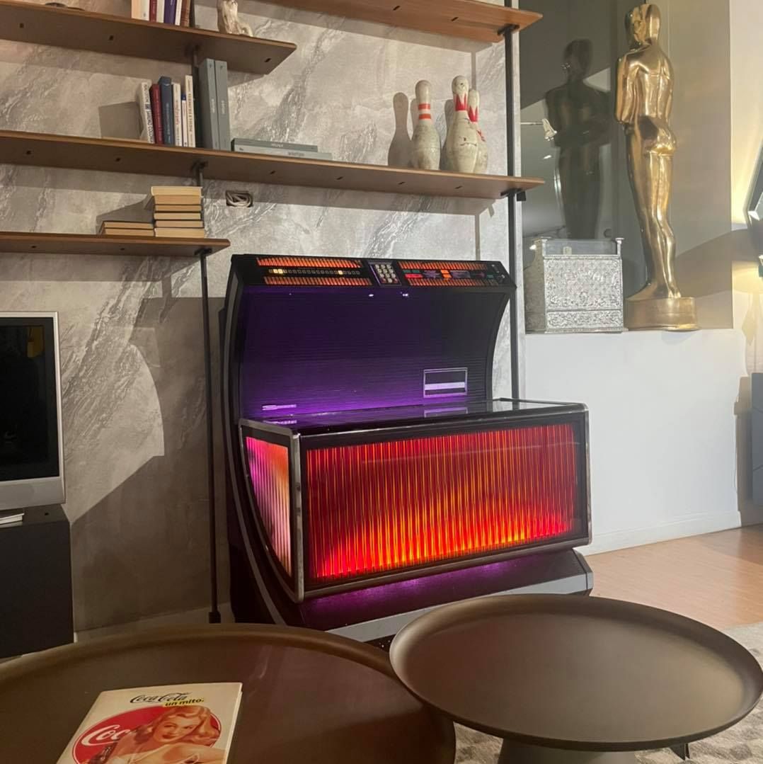 Jukebox vintage illuminato in viola e rosso, con ripiani in legno e birilli sullo sfondo.