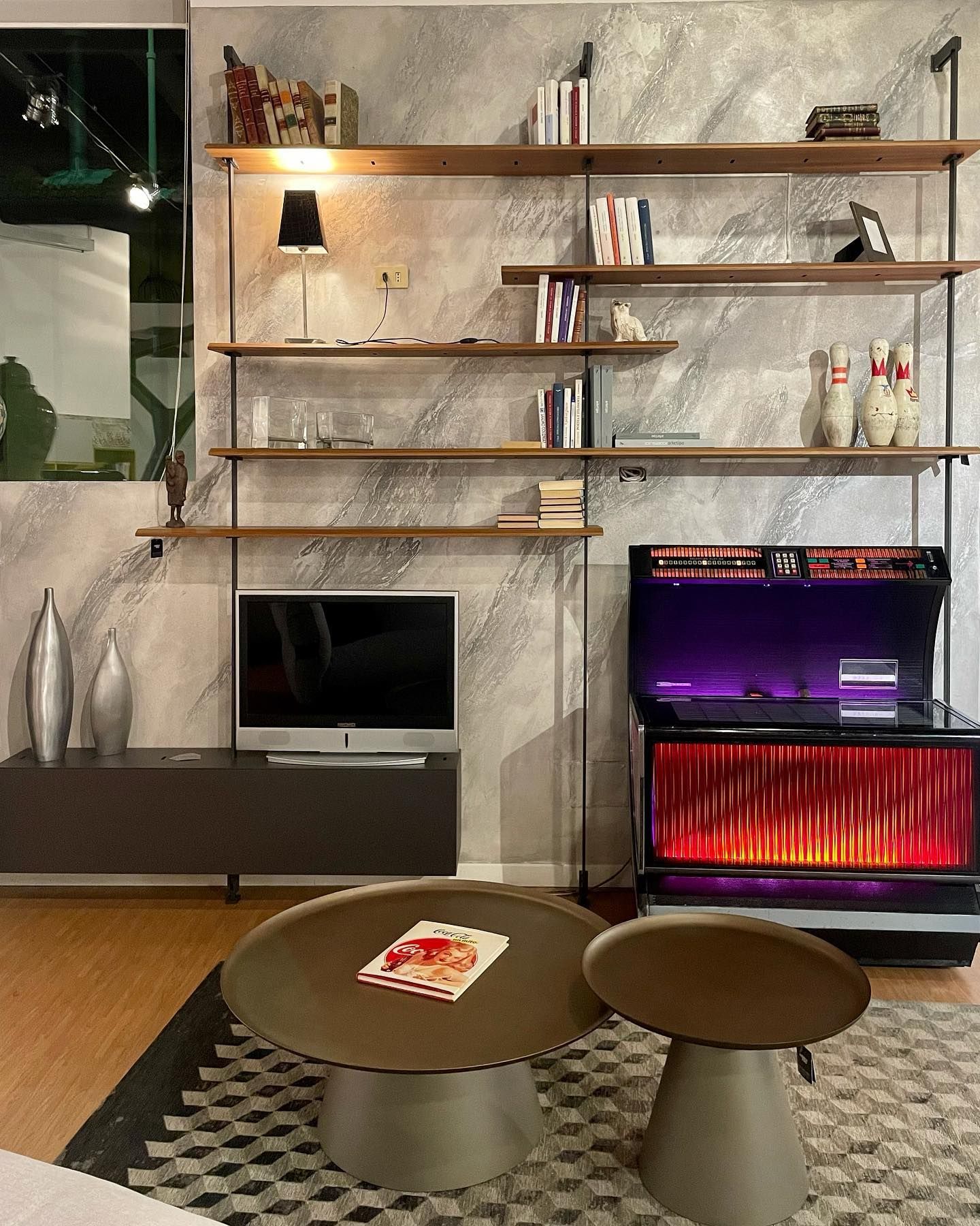 Soggiorno con scaffalature, TV, jukebox e tavolini da caffè.