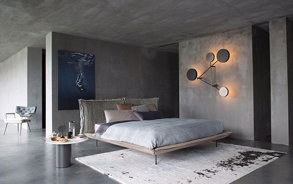 Moderna camera da letto grigia con letto, opere d'arte, tappeto e lampade da parete scultoree.