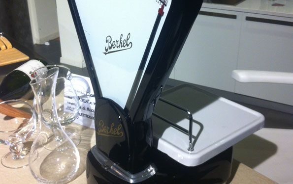 Bilancia Berkel bianca e nera con vassoio bianco, vicino a una caraffa e dei bicchieri.