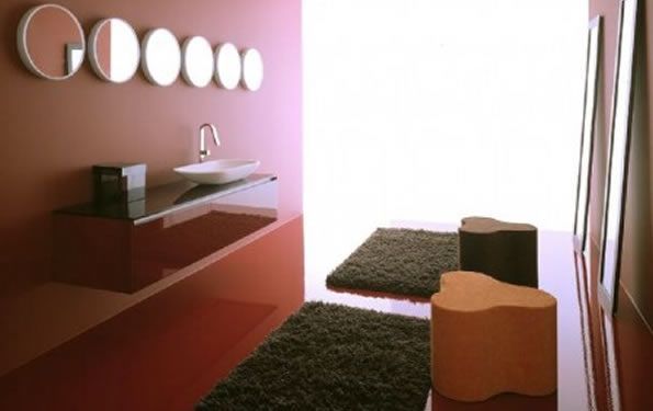 Bagno moderno con pareti rosse, specchi ovali, lavandino sospeso, tappeti scuri e sgabelli.