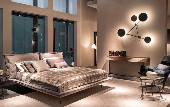 Camera da letto moderna con letto grande, illuminazione a parete di design e tavolino laterale.