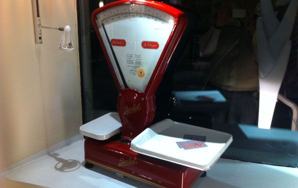 Bilancia vintage rossa e bianca con due vassoi, esposta in una vetrina.