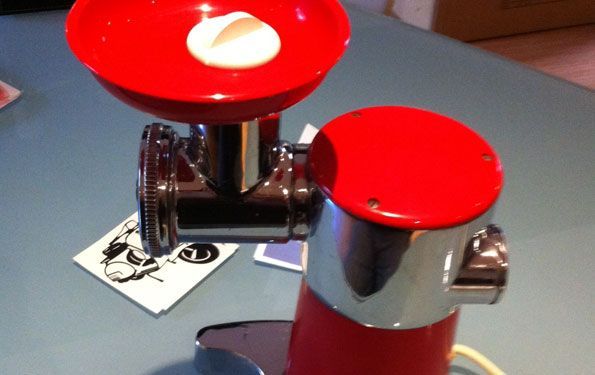 Tritacarne elettrico rosso e cromato su una superficie blu, cibo nella tramoggia.