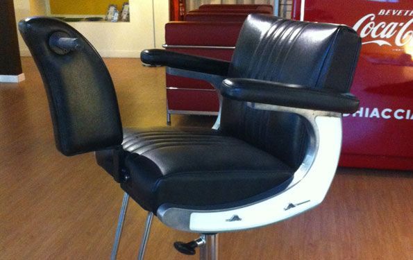 Poltrona da barbiere in pelle nera con finiture argentate in un salone.