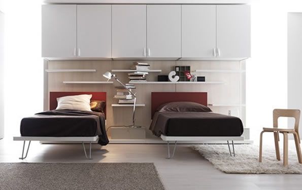 Camera da letto moderna con due letti, testiere rosse, mobili contenitori bianchi e una sedia.