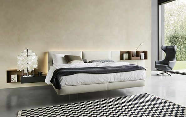 Camera da letto moderna con letto a piattaforma, mensole sospese, tappeto e poltrona decorativa.