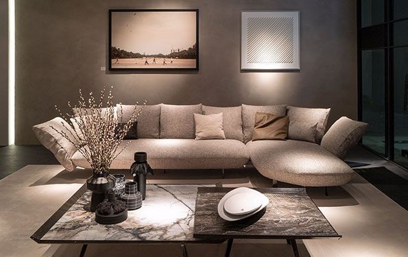 Soggiorno con divano componibile beige, tavolino da caffè, opere d'arte e illuminazione ambientale.