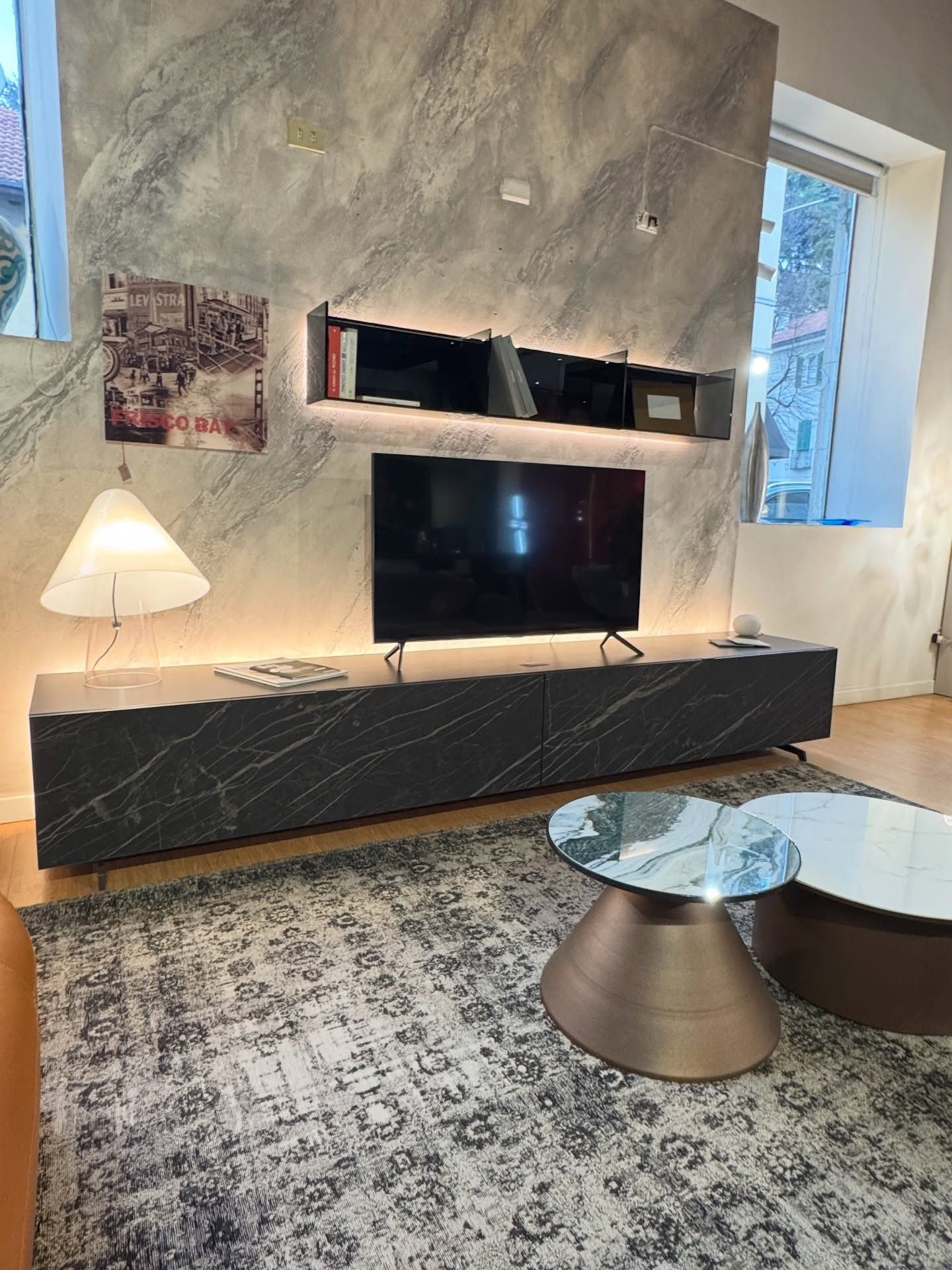 Soggiorno moderno con mobile TV effetto marmo grigio, televisore e tavolini da caffè su un tappeto a fantasia.
