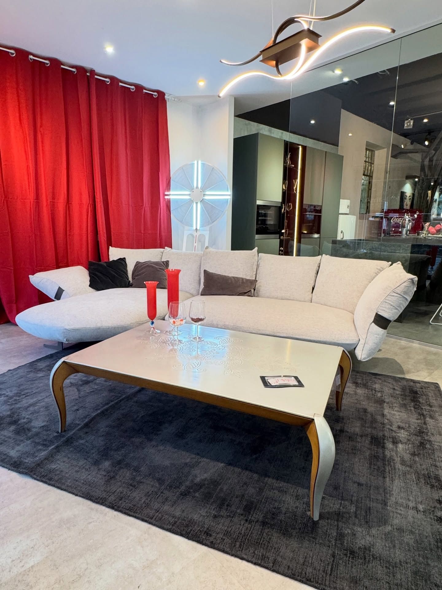 Soggiorno con divano bianco, tende rosse e tavolino rettangolare su tappeto grigio.