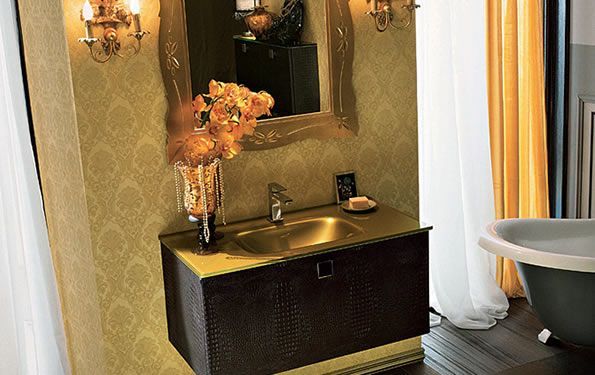 Bagno nei toni dell'oro con specchio decorato, lavandino e fiori. Mobiletto nero, pareti gialle e vasca da bagno a vista.