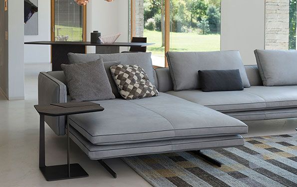 Divano componibile grigio con cuscini e tavolino in un soggiorno moderno.