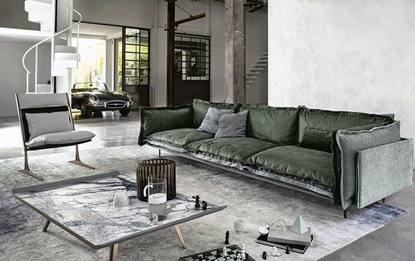 Divano in velluto verde in un soggiorno moderno con poltrona grigia, tavolino in marmo e scala a chiocciola.