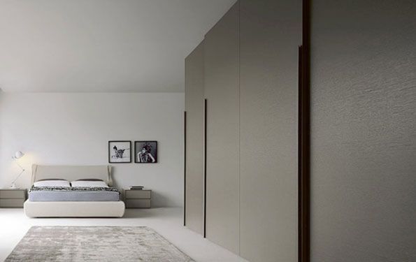 Camera da letto con ampio armadio dai toni neutri, letto, comodini, tappeto e quadri incorniciati su pareti bianche.