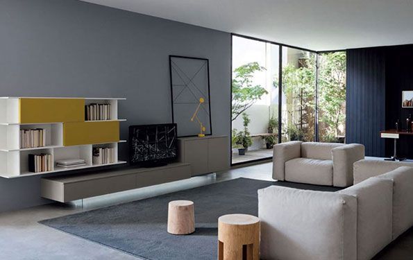 Soggiorno moderno con spazio contenitore incorporato grigio e giallo, divano neutro e ampie finestre che si affacciano sul cortile.