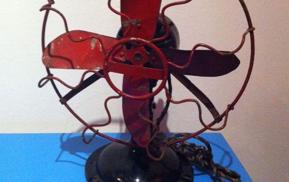 Ventilatore elettrico vintage rosso e nero con pale a vista e gabbia metallica.