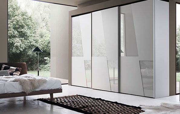 Moderno armadio bianco con design astratto; camera da letto con letto, tappeto e ampia finestra.