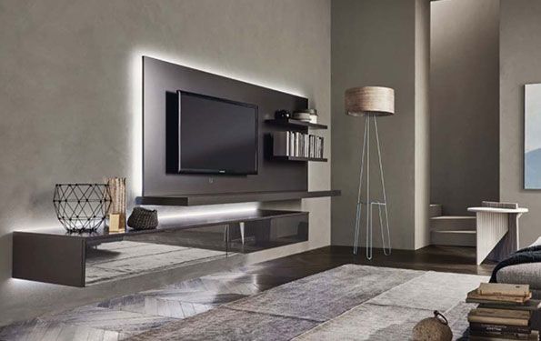 Soggiorno moderno con TV a parete, mensole e mobili grigi a filo pavimento. Pareti grigio chiaro con tappeto e lampada alta.