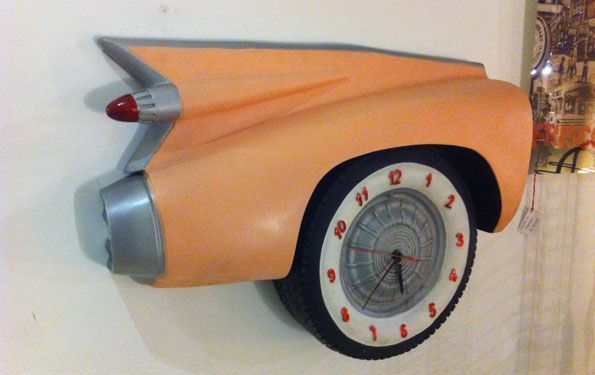 Orologio da parete arancione a forma di auto d'epoca con quadrante bianco e numeri e lancette rossi.