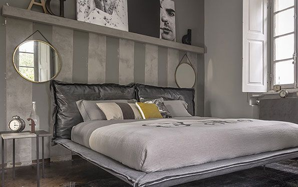 Camera da letto con testiera a strisce grigie, letto, specchi, quadri e finestra.