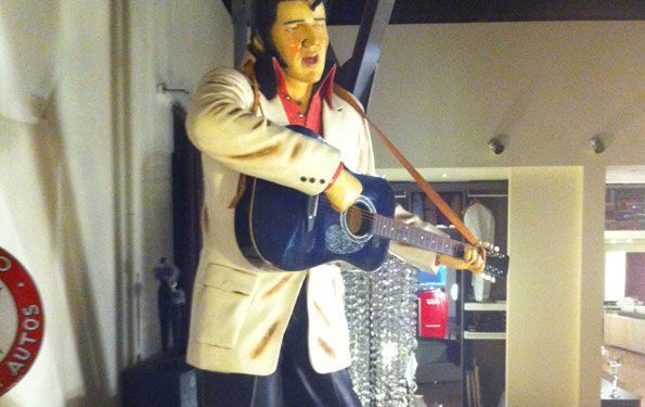 Statua di Elvis Presley che suona una chitarra blu, indossa un abito bianco e canta.