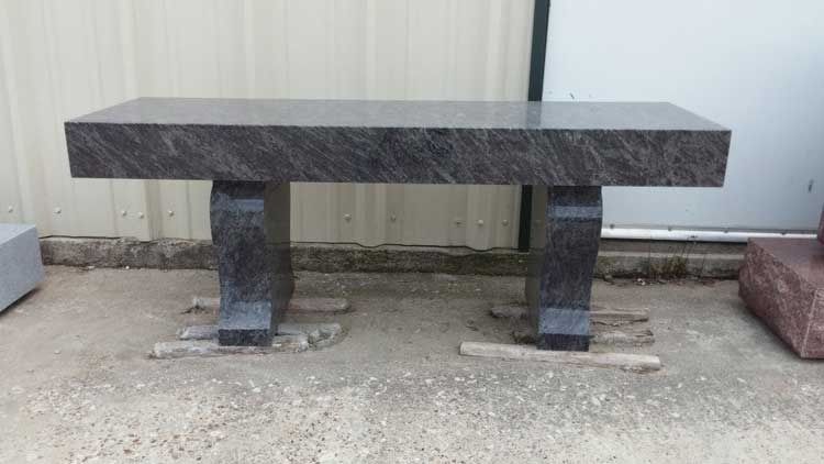 Dark stone bench on concrete ground against a light corrugated wall.