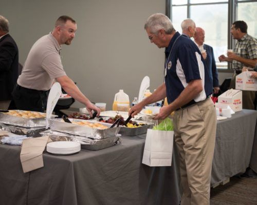 A group of men are standing around a table serving food.