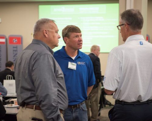 A group of men are standing in a room talking to each other.