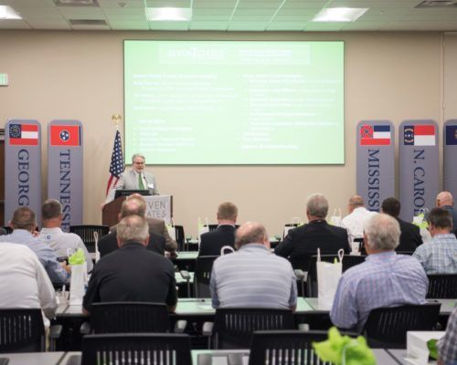 A man is giving a presentation to a group of people in front of a screen that says mississippi on it
