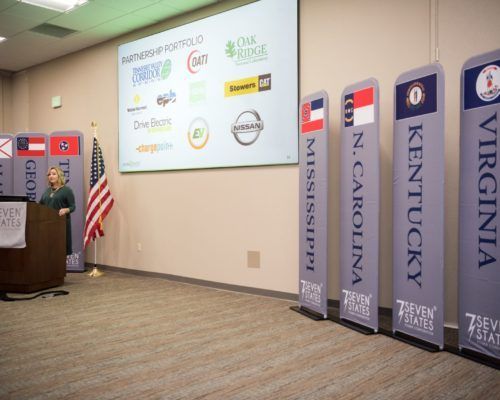 A woman is standing at a podium in front of a large screen.