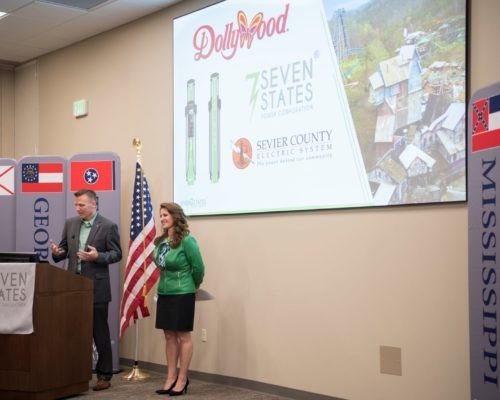 A man and a woman are giving a presentation in front of a large screen.