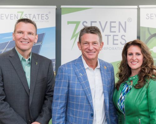 Three people are posing for a picture in front of a seven states sign.