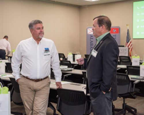 Two men are standing in a room talking to each other.