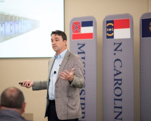 A man in a suit is giving a presentation in front of n. carolina signs