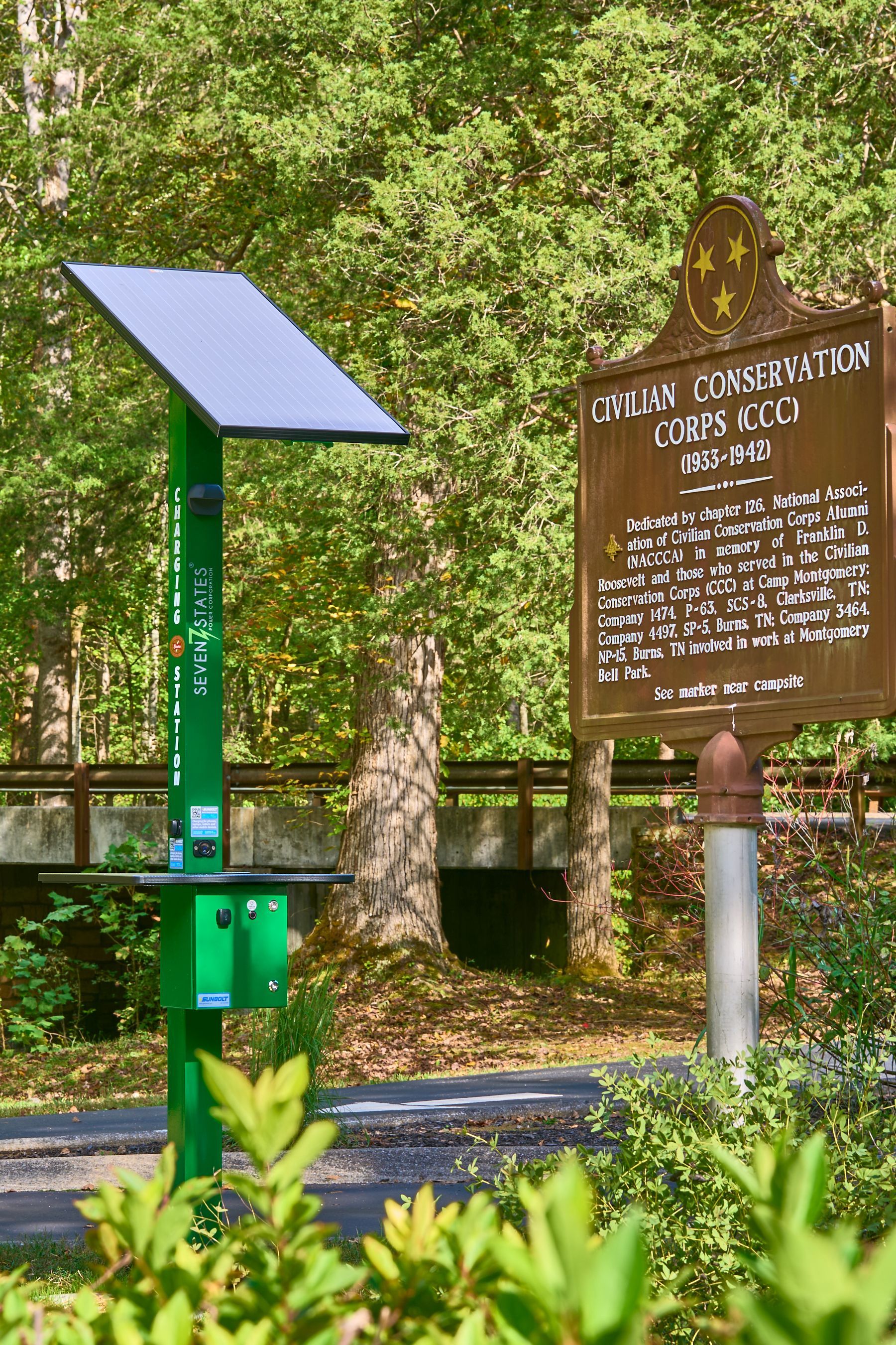 A green box with a solar panel on top of it is next to a wooden sign.