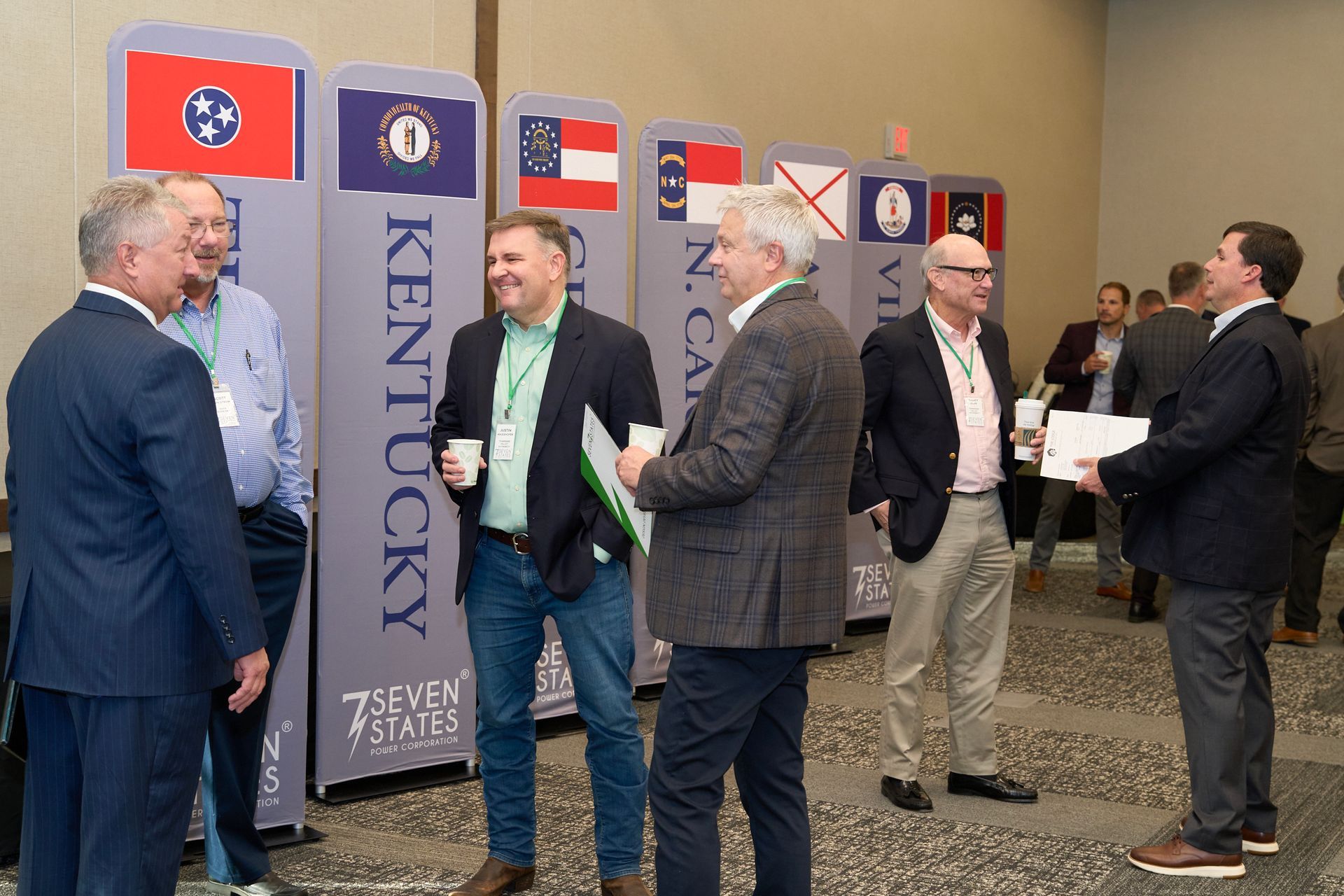 A group of men are standing in a room talking to each other.