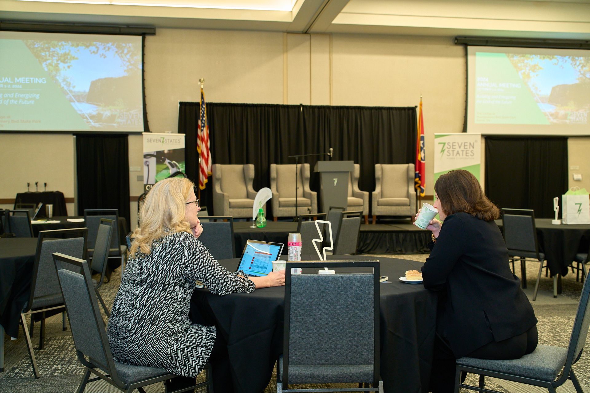 Two women are sitting at a table in a conference room.