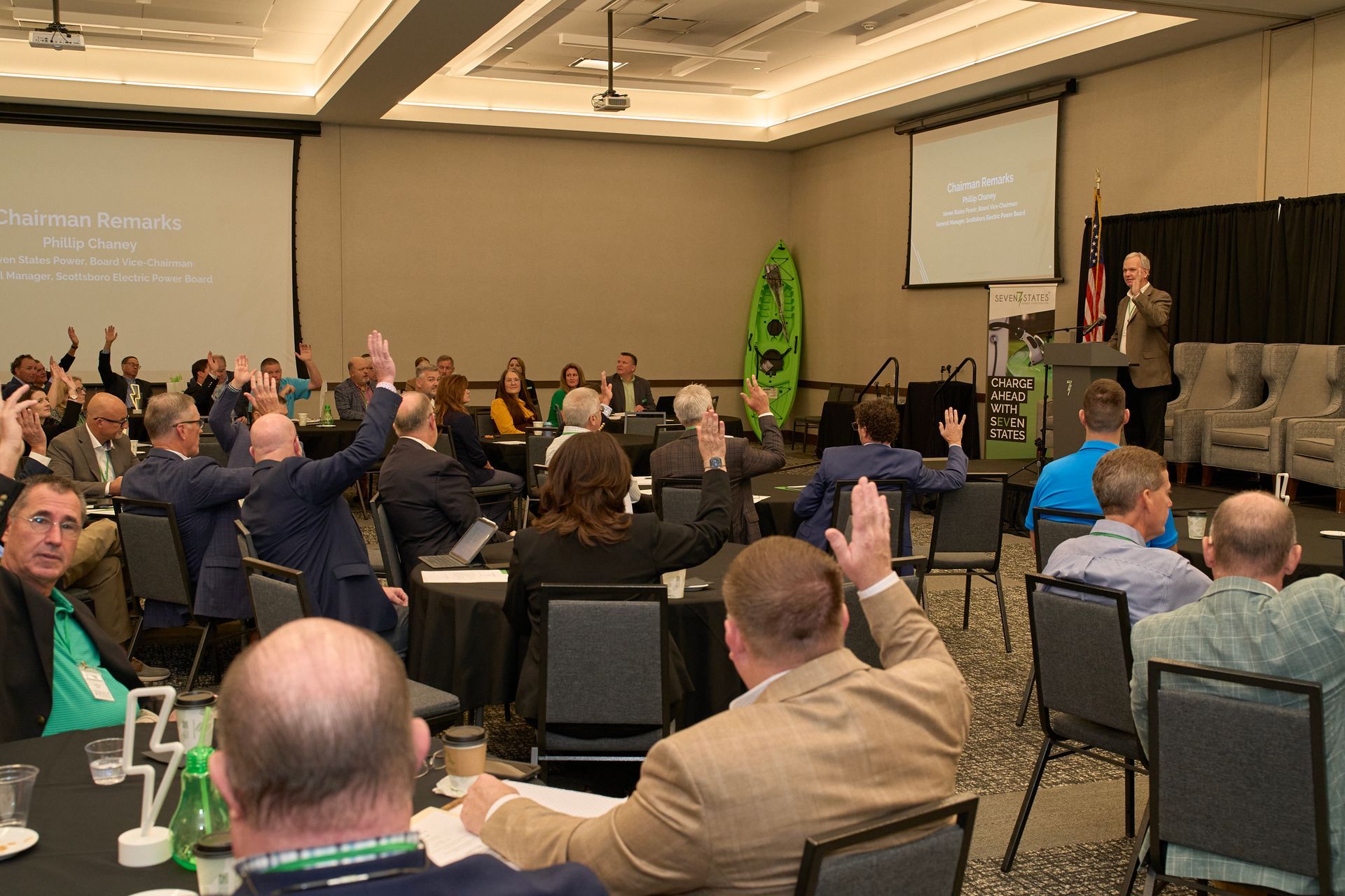 A group of people are sitting in a conference room raising their hands.