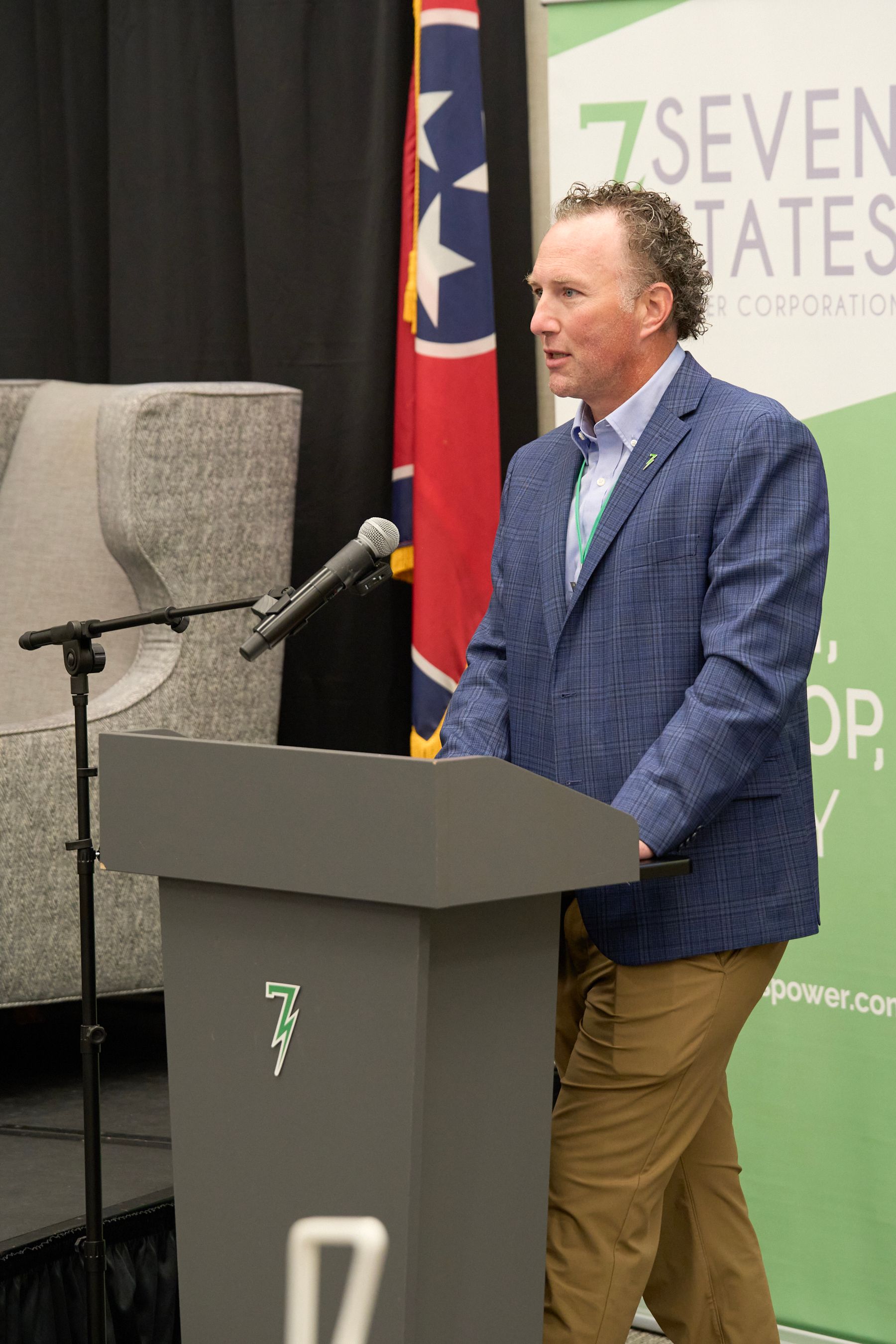 A man in a blue suit is standing at a podium speaking into a microphone.