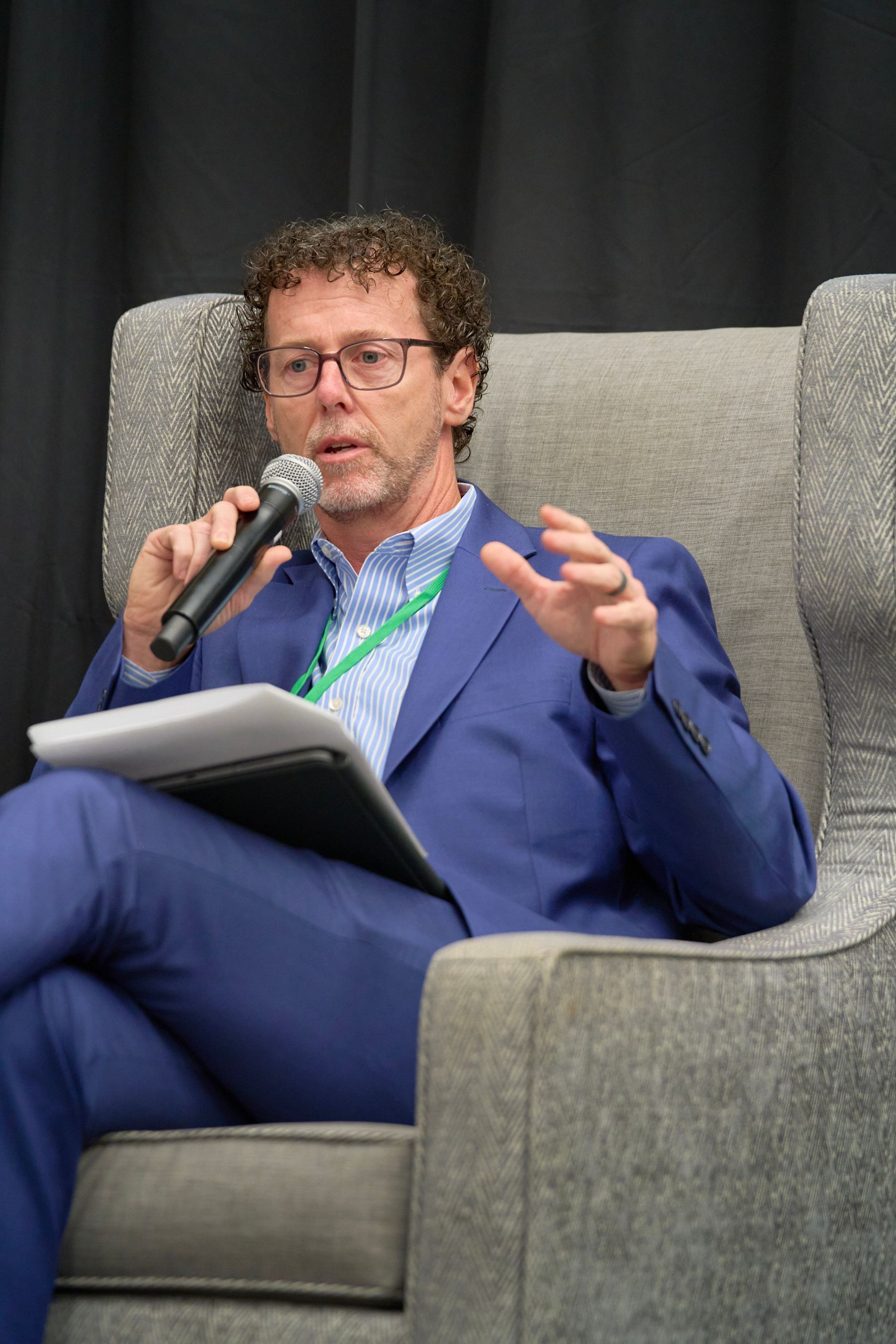 A man in a suit is sitting in a chair holding a microphone.