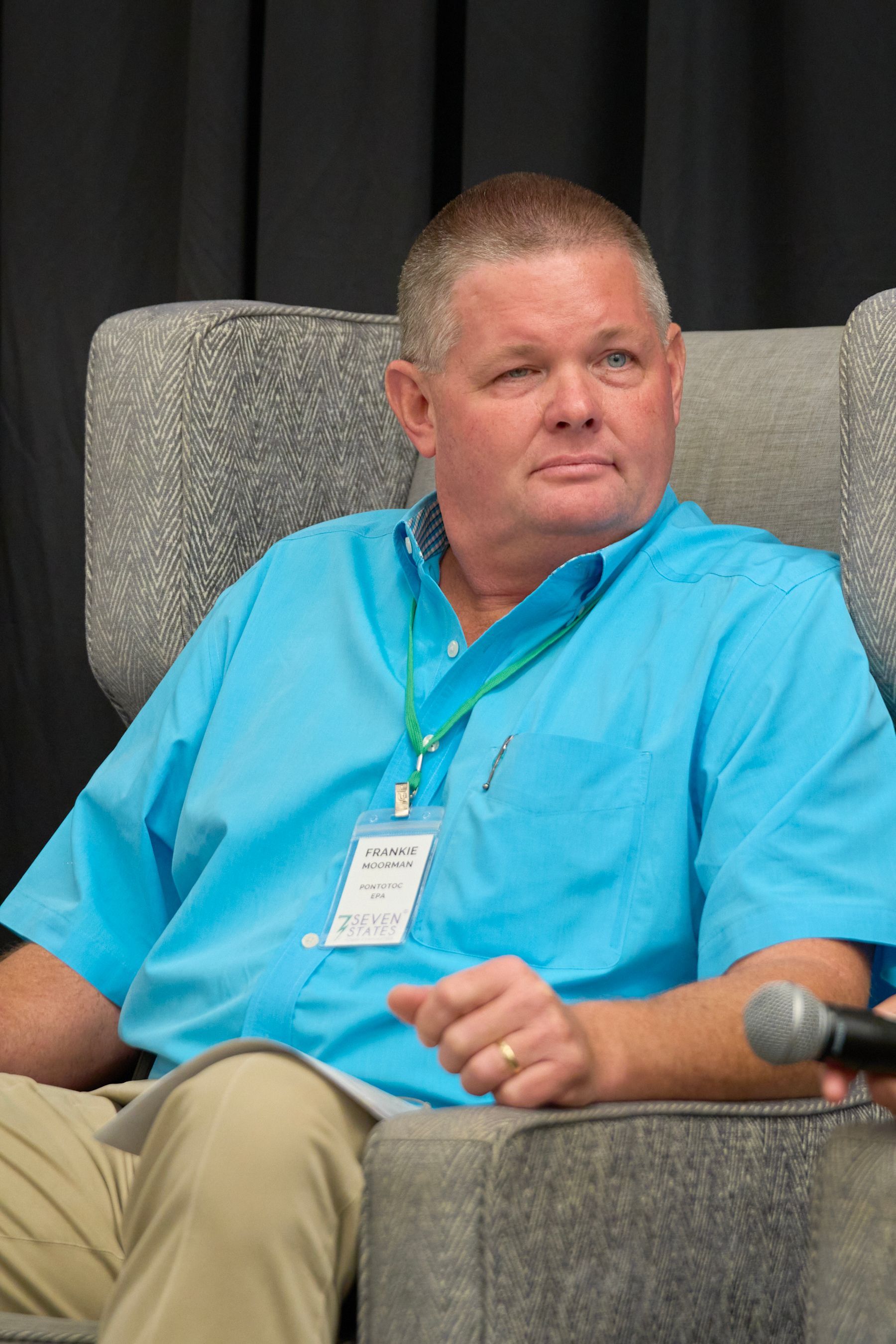 A man in a blue shirt is sitting in a chair with a microphone.
